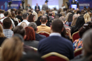 Shallow depth of field (selective focus) details with a crowd of people attending a conference indoors.