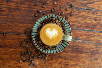 A glass of hot latte coffee with heart latte art in striped handmade ceramic cup on wooden table background.
