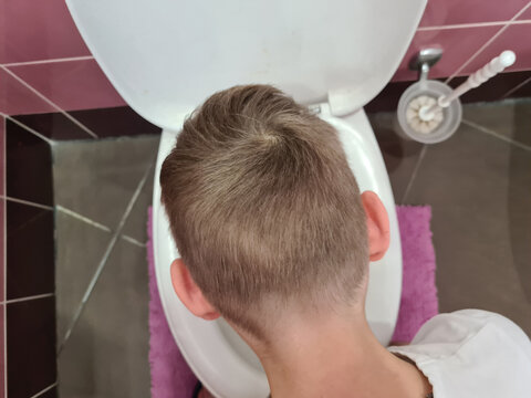 Sick child boy vomits into toilet bowl