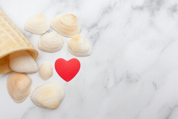 On a marble background, an ice cream cone with shells and a red heart. Place for text. Copy space. Time for vacation and rest. Flat lay. Top view.