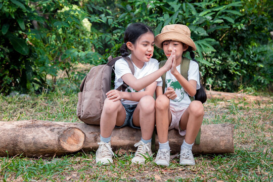 Asian boys and girl children wearing plaid T- shirt save world banner and backpack sitting at tree base talking and stack of hands is holiday teamwork travel concept.