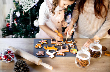 Happy little girl with her beautiful mom coloring Christmas gingerbread cookies at home. Christmas...