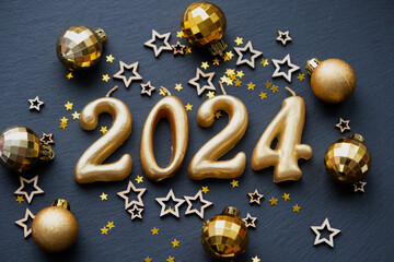 The golden figures 2024 made of candles on a black stone slate background are decorated with a...
