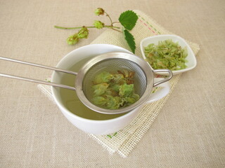 Herbal tea with dried hop flowers in tea strainer
