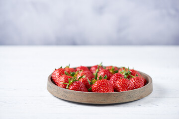 Fresh red strawberries in a grey ceramic plate on a white wooden table. Horizontal, copy space, close-up.