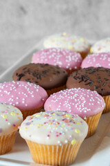 Cupcakes, decorated with icing and sprinkles on a white serving plate. On a concrete background
