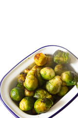 Brussels sprouts, oven roasted in olive oil,  in an enamel dish bowl. Isolated on a white background