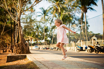 Fototapeta na wymiar Happy little caucasian girl five years old walking on the city road on sunset at summer evening