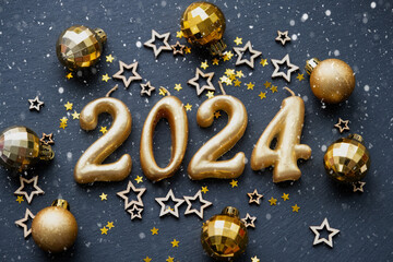 The golden figures 2024 made of candles on a black stone slate background are decorated with a...