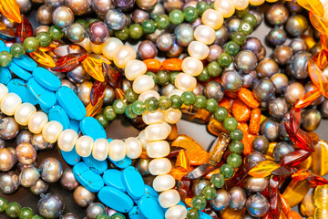 Beads and necklaces made of colored semi precious stones. Background from a variety of beautiful jewelry, multi-colored turquoise stones, amber, cat's eye, pearls.