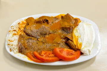 Traditional turkish iskender kebab in copper plate with yogurt, grilled tomatoes and fresh vegetables.