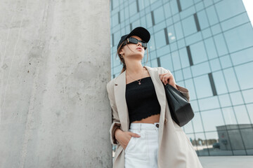 Fashionable urban beautiful woman model with a cool cap and black sunglasses with casual fashion...