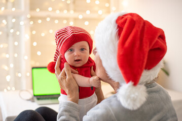 Little child  in striped hat and red t-shirt and Grandmother in santa hat. Woman holds and talking with kid. Happiness and love. Wonderful Christmas and New year holidays.