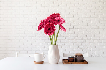Bright gerbera daisies in white vase on kitchen table, minimal style toned with viva magenta © dark_blade