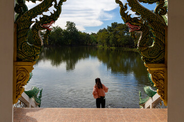 Tourists feed fish at a riverside pavilion with Naga statues decorating the pillars of a beautiful...