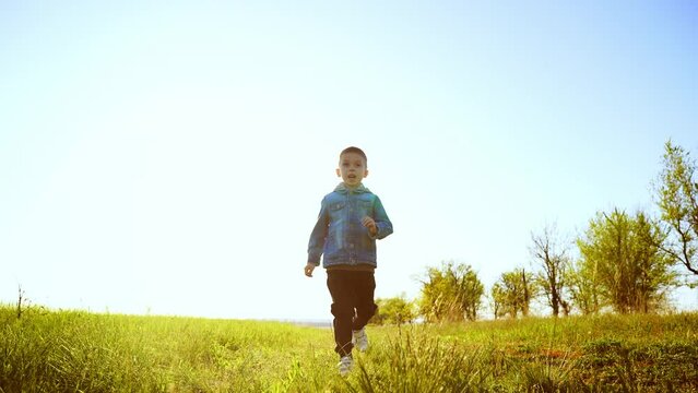 A happy boy runs through the green park on a warm summer day. Cheerful childhood.