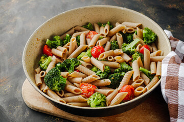 delicious penne wheat pasta with tomatoes, broccoli and mozzarella on a dark background