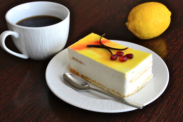 creamy lemon slice of cake on white saucer with teaspoon and cup of coffee isolated, close-up