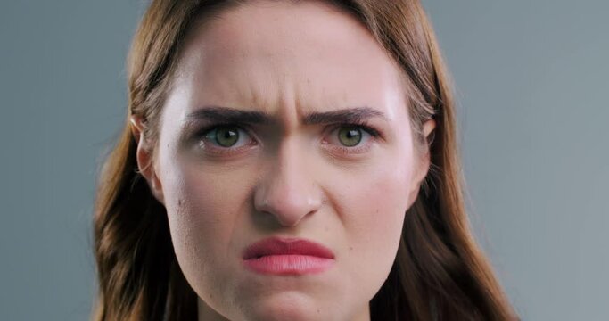 Displeased woman looking at camera on light grey background, closeup