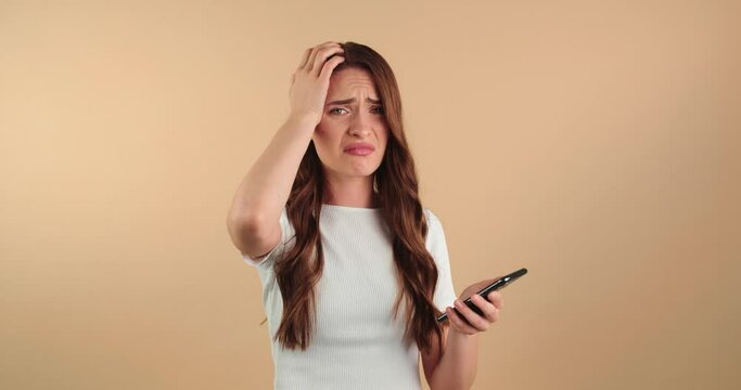 Unhappy young woman with mobile phone got bad news. Beige background