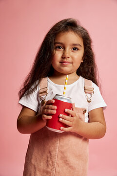 Portrait of beautiful little girl, child, posing, driking lemonade isolated over pink background. Concept of childhood, fashion, emotions