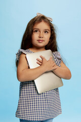 Portrait of cute little girl, child, posing with tablet isolated over blue background. Concept of childhood, fashion, emotions