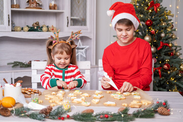two kids boy and girl in pajamas cooking festive gingerbread in christmas decorated kitchen