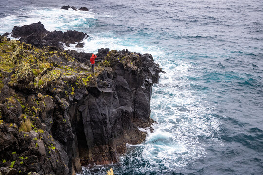 Man standing on dark volcanic rock at the coast of São Jorge, Azores 