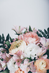 Beautiful bouquet of fresh colorful pastel ranunculus and lily flowers in full bloom with green fern leaves against white background, close up. Spring bunch of blossoms. Copy space.