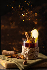 Christmas drink. Mulled wine  decorated with apple and with spices on wooden cut board witj golden bokeh. Winter time beverage  concept.