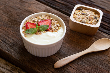 trawberry yogurt in a wooden bowl with granola, honey, mint and fresh strawberry on wooden background. Health food concept.