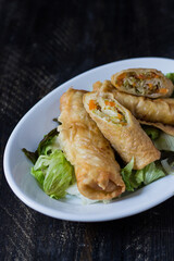 Homemade spring rolls on a bed of lettuce. In a white plate on a wooden background