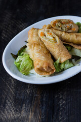 Homemade spring rolls on a bed of lettuce. In a white plate on a wooden background