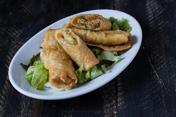 Homemade spring rolls on a bed of lettuce. In a white plate on a wooden background