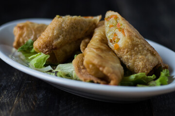 Homemade spring rolls on a bed of lettuce. In a white plate on a wooden background