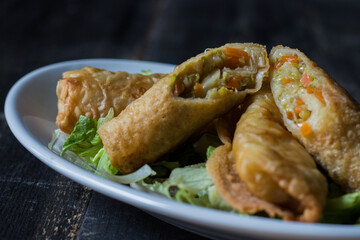 Homemade spring rolls on a bed of lettuce. In a white plate on a wooden background