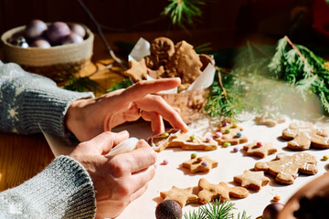 Woman's hands decorating glazed christmas gingerbread cookies a shape of gingerbread man,christmas tree and star,decorated with colorful sugared almonds.Christmas and New Year traditions festive food.