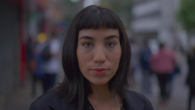 Closeup woman with indigenous traits standing in urban street sidewalk looking at camera with serious expression. South American latina female person