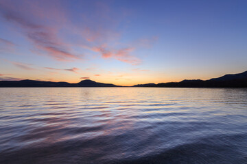 Fototapeta na wymiar グラデーションの空の雲がピンク色に染まる夜明けの湖。