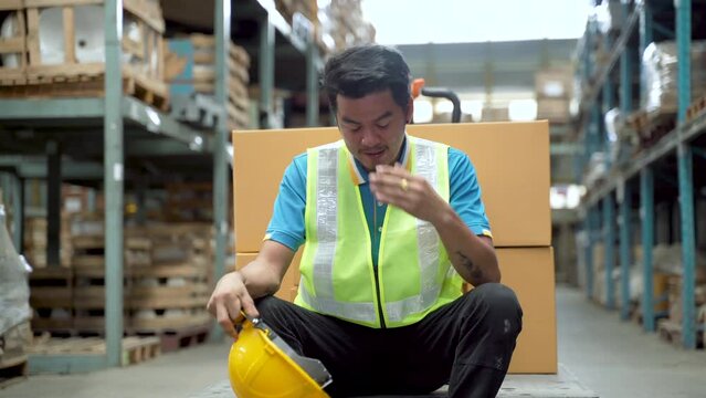 4K, Employees working in a large warehouse with racks to the side sit in the workforce to relax from the heat and exhaustion. Sit back and take off your hat to relieve fatigue.