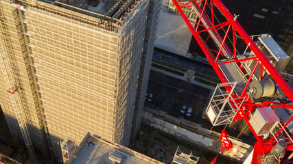 Aerial view of a red and white industrial tower crane operating in high building construction site. These large machines allow the concrete plates weight balance. City development concept.