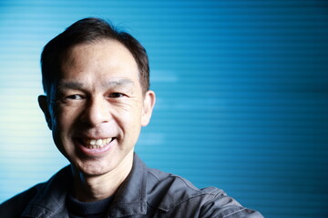A craftsman poses in gray work clothes in front of blue shutter of a factory. Conceptual images of the essence of manufacturing, technical succession and the challenge of high-precision machining.