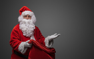 Shot of bearded santa with huge bag and red costume posing with his hand.