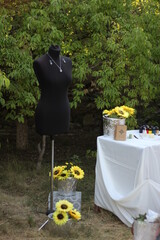 Black mannequin among the trees, table with white athals tablecloth with sunflower flowers