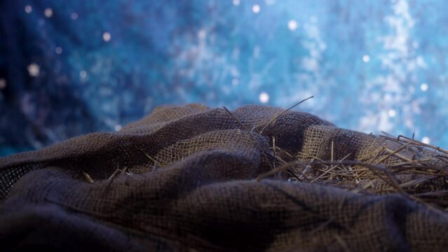A manger with burlap in hay with starry skies in the background.