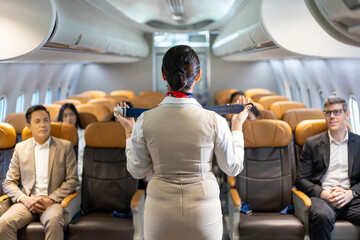Asian flight attendant is demonstrating safety procedure using seat belt before taking off in the...