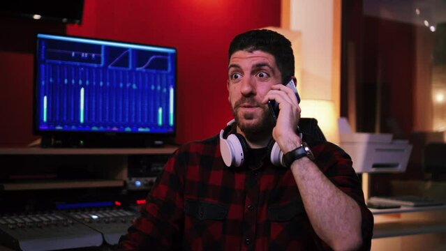 Close up view of happy sound engineer or male entrepreneur having a business call sith customer artist in a professional music studio talking about the equalization of the track. High quality 4k