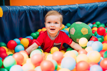 Happy laughing boy 1-2 years old having fun in ball pit  in kids amusement park and indoor play...