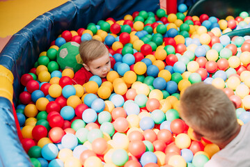 Happy laughing boy 1-2 years old having fun in ball pit  in kids amusement park and indoor play...