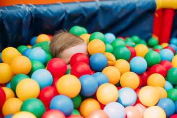 Happy laughing boy 1-2 years old having fun in ball pit  in kids amusement park and indoor play center. Activity toys for little kid